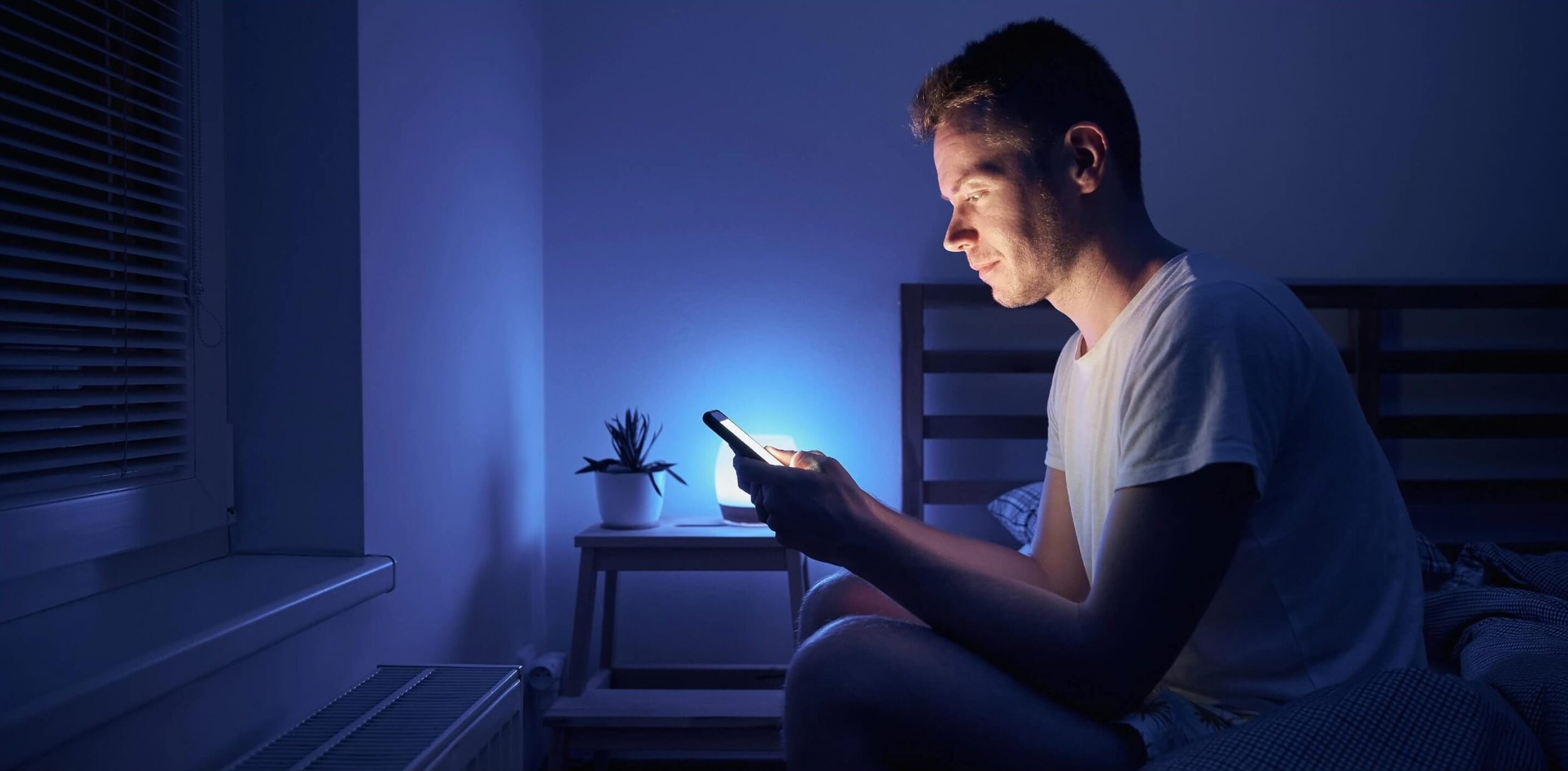 man-sitting-in-bedroom-and-using-phone-at-night-2022-01-04-22-33-32-utc@2x-scaled-e1697543260238